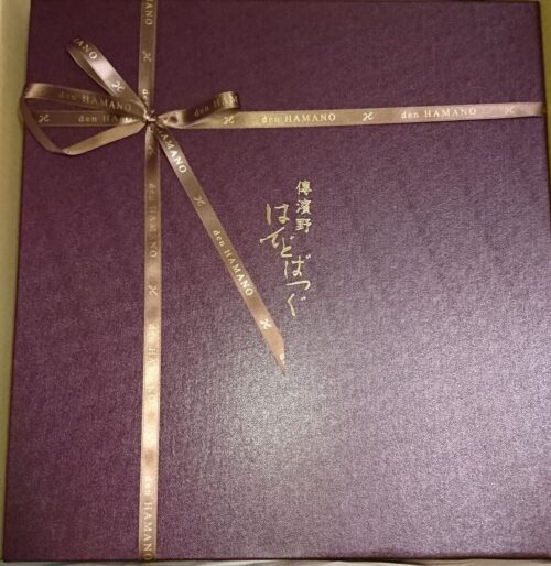 濱野バッグ《ミーティア》が入っていた赤紫色の化粧箱。リボンが掛けられ、中央に「傳濱野はんどばっぐ」のロゴが印字されている。