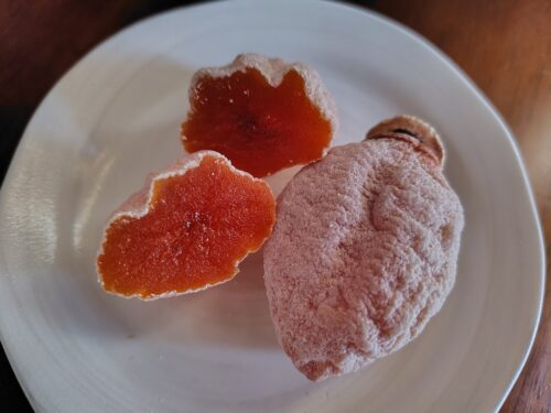 お皿に盛りつけられた市田柿。1個は丸ごと、もう1個は半分に切ってあり、鮮やかなオレンジ色が見える。